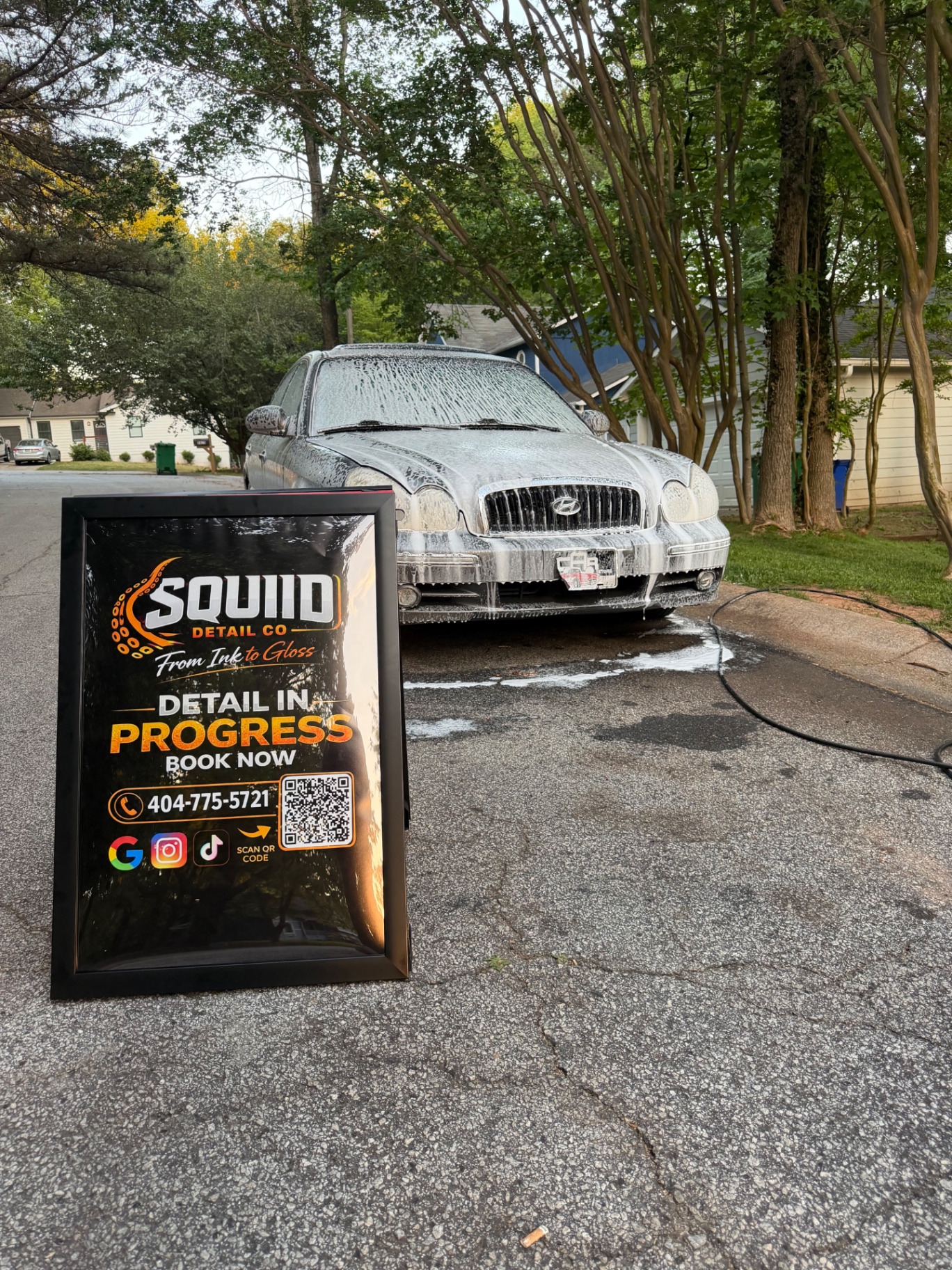 Squiid Detail Co sign beside a foam-covered sedan during wash